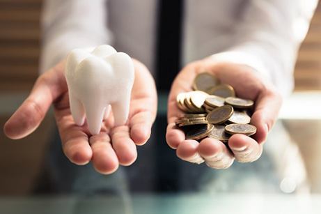 Hands holding a large model tooth and a pile of coins