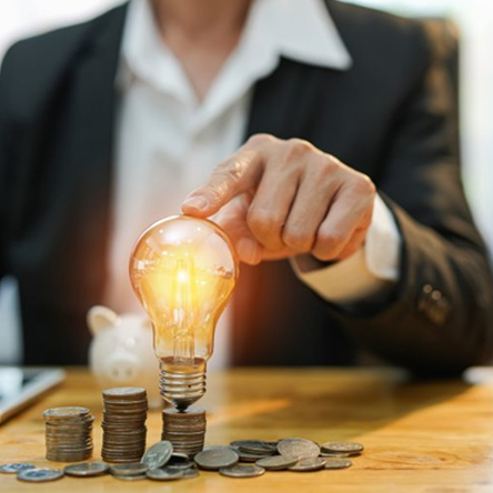 Man tapping a lightbulb that’s sitting on a stack of coins
