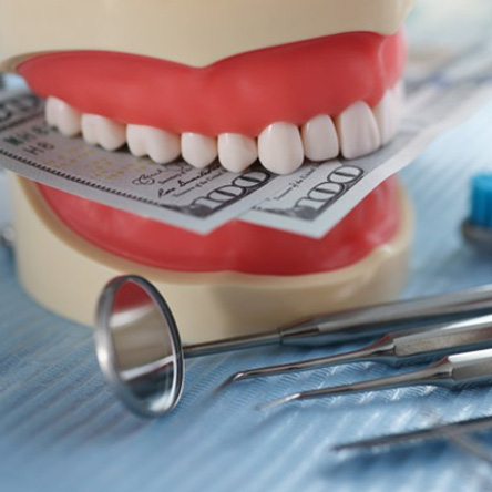 A model of teeth chomping down on paper money and sitting next to several dental tools
