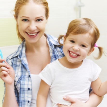 Woman holding little girl in one hand and toothbrush in other