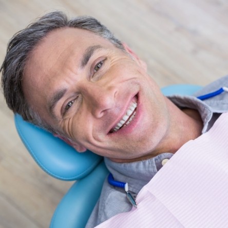 Grey haired man sitting back in dental chair and smiling