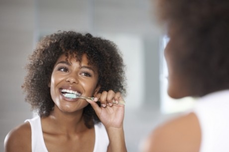 Woman brushing her teeth in bathroom mirror