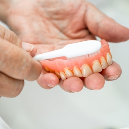 Closeup of dentures in hand being brushed