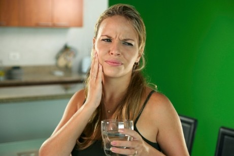 Woman with glass of water rubbing tooth in pain