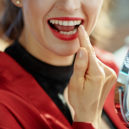 Woman pointing to teeth while looking in small mirror