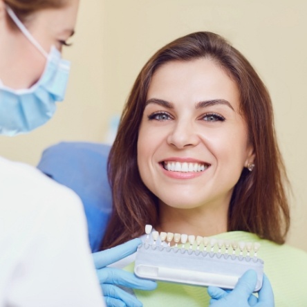 Female patient smiling while dentist holds shade matching tabs 