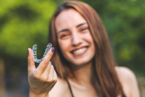 Woman smiling while holding up her Invisalign
