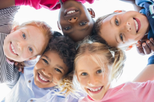 Children huddling in a circle and smiling down at camera view